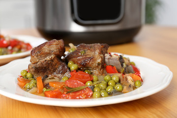 Plate with meat and garnish prepared in multi cooker on table, closeup