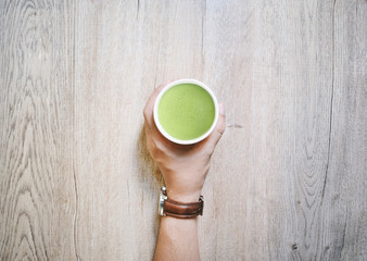 hand holding  paper cup of Matcha Green Tea Latte on wooden background. 