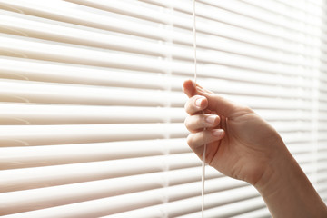 Woman opening window blinds, closeup. Space for text