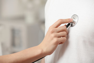 Doctor examining patient with stethoscope against blurred background, closeup