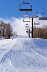 A lone skier descends a groomed run with a chairlift at a ski hill