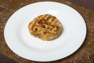 Meat roast cutlet on a white plate on a brown background.