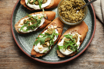 Plate with tasty bruschettas and pesto sauce on wooden table, top view