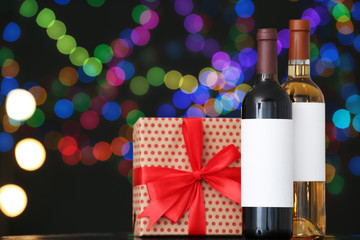 Gift box with and bottles of wine on table against blurred lights, space for text. Bokeh effect