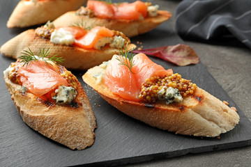 Tasty bruschettas with salmon and blue cheese on slate plate, closeup