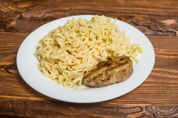 Meat roast cutlet with boiled pasta, spaghetti on a wooden background. Simple fast food.