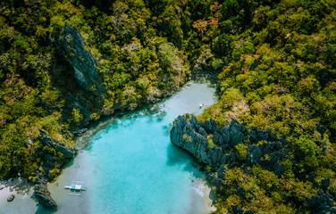 Aerial drone view of blue turquoise transparent lagoon water of tropical island with rugged steep mountains rocks, jungle and sandy beaches