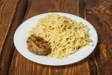 Meat roast cutlet with boiled pasta, spaghetti on a wooden background. Simple fast food.