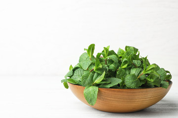 Wooden bowl with fresh green mint on table. Space for text