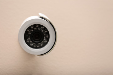 Modern CCTV security camera on beige wall. Space for text