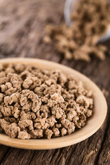 Raw dehydrated soy meat, soy protein, soya chunks or textured vegetable protein on wooden plate, photographed on rustic wood (Selective Focus, Focus in the middle of the soy meat)