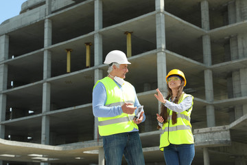 Professional engineer and foreman with tablet in safety equipment at construction site. Space for text.