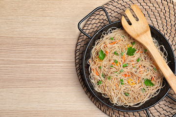 Top view of pan with delicious asian noodles and vegetables on wooden background. Space for text