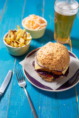 Delicious homemade burger with french fries and salad (coul slow) on a blue table with forks and knife