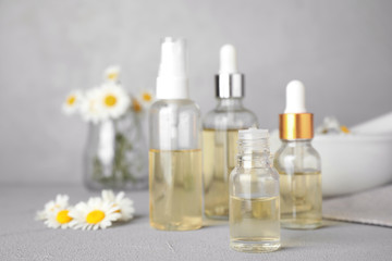 Bottles of chamomile essential oil and flowers on grey table, space for text
