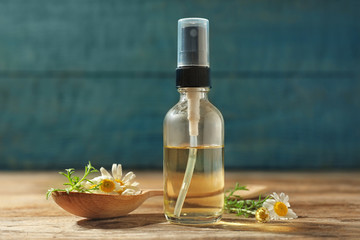 Bottle of chamomile essential oil and spoon with flowers on wooden table