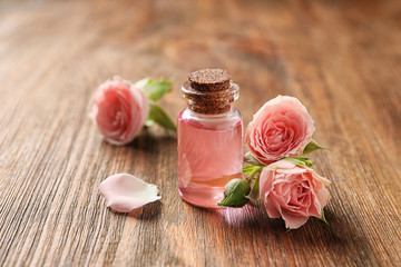 Obraz na płótnie Canvas Bottle of rose essential oil and flowers on wooden table