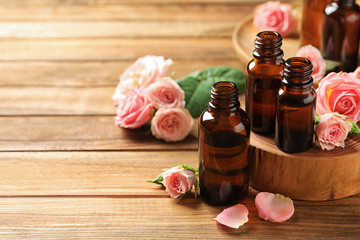 Obraz na płótnie Canvas Bottles of rose essential oil and fresh flowers on wooden table, space for text