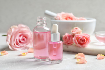 Fototapeta na wymiar Bottles of rose essential oil and fresh flowers on table