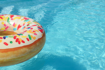 Bright inflatable doughnut ring floating in swimming pool on sunny day. Space for text