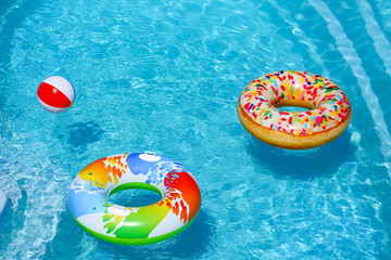 Bright inflatable rings and beach ball floating in swimming pool on sunny day