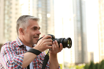 Fototapeta na wymiar Handsome mature man taking photo with professional camera outdoors. Space for text
