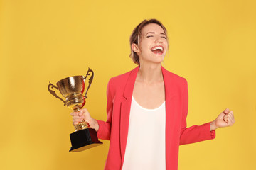 Portrait of happy young businesswoman with gold trophy cup on yellow background