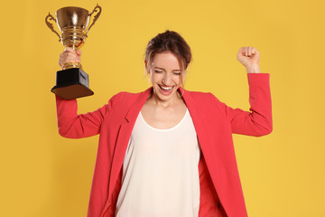 Portrait of happy young businesswoman with gold trophy cup on yellow background