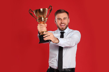 Portrait of happy young businessman with gold trophy cup on red background