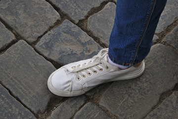 foot in a white sneaker on a stone sidewalk