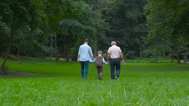 Family Generations concept: Father, son and Granddad, outdoors, in Nature, enjoying their Quality Time together, All in nice wear take child to school. Back view.