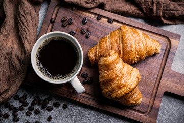 Breakfast with fresh croissants and cup of black coffee on wooden board