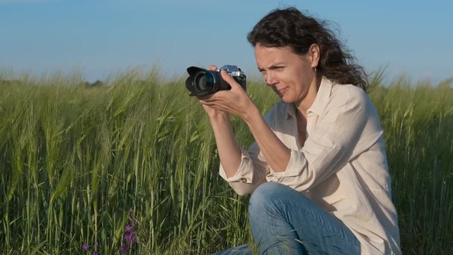 Happy woman taking pictures of wheat. Pretty woman with a camera in nature.