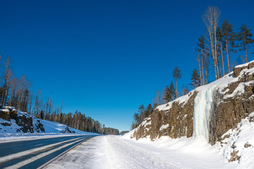 Karelia. Russia. Frozen waterfall along the road. Karelian waterfalls. The road between snow-covered rocks. Ruskeala. Northern nature of Karelia. Travelling to Russia.