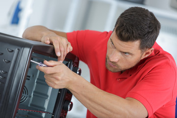 repairman with screwdriver fixing oven in kitchen