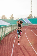 Sport. Athletic young brunette woman in pink sneakers, leggings and top run on running track stadium at sunset. her hair is developing. Concept run. concept of a healthy lifestyle