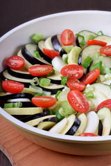 Raw zucchini, eggplants and cherry tomatoes in a baking dish ready for roasting