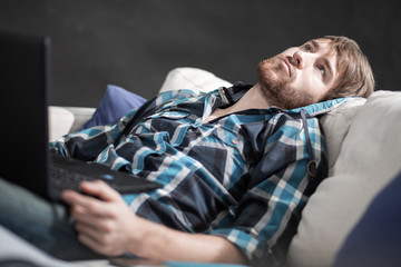 Tired hipster man lying on couch and looking into space