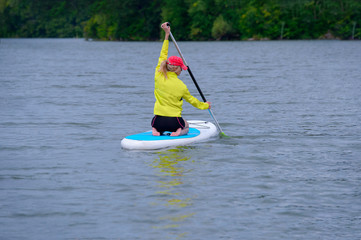 rear view of girl with blue hair sitting on paddle board on river