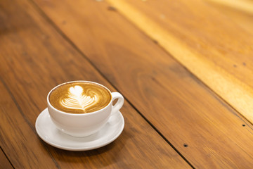 Close up of white cup of hot coffee latte with heart shape and flower art on wooden table and copy space.