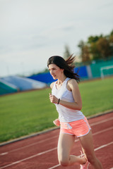 Portrait of girl running track on stadium. Real front view of young woman in pink shorts and tank top and pink sneakers. Outdoors, sport