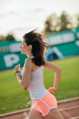 Girl running track on stadium. Real front view of young woman in pink shorts and tank top and pink sneakers. Outdoors, sport. side view