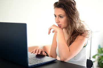 Fototapeta premium Cute girl surprised by something while working at home from behind her laptop