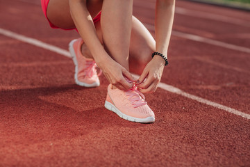 Young woman hands tie laces on her pink sport shoes on a stadium on a running path. White stripe near her. Close-up of tying shoes