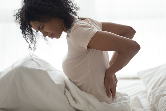 Sad young african woman touching back feeling backache in bed