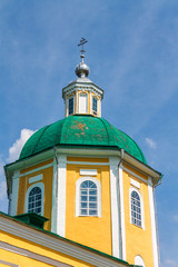 Fototapeta na wymiar Yellow Orthodox Christian church with a green dome in summer against a blue sky with white clouds.
