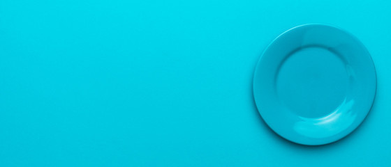 Top view photo of empty blue plate. Panoramic image of round ceramic plate over turquoise blue background with copy space and right side position. Mockup of blank dish on blue table.