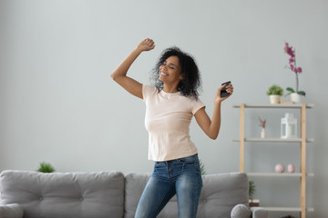 Smiling active black woman dancing alone holding phone at home