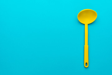 Top view photo of vivid plastic kitchen utensil. Minimalist flat lay image of yellow ladle over turquoise blue background with copy space. Right side position of dipper on blue table.