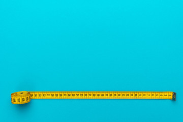 Top view of yellow soft measuring tape. Minimalist flat lay image of tape measure with metric scale over turquoise blue background with copy space. Photo of body measuring tape as diet concept.